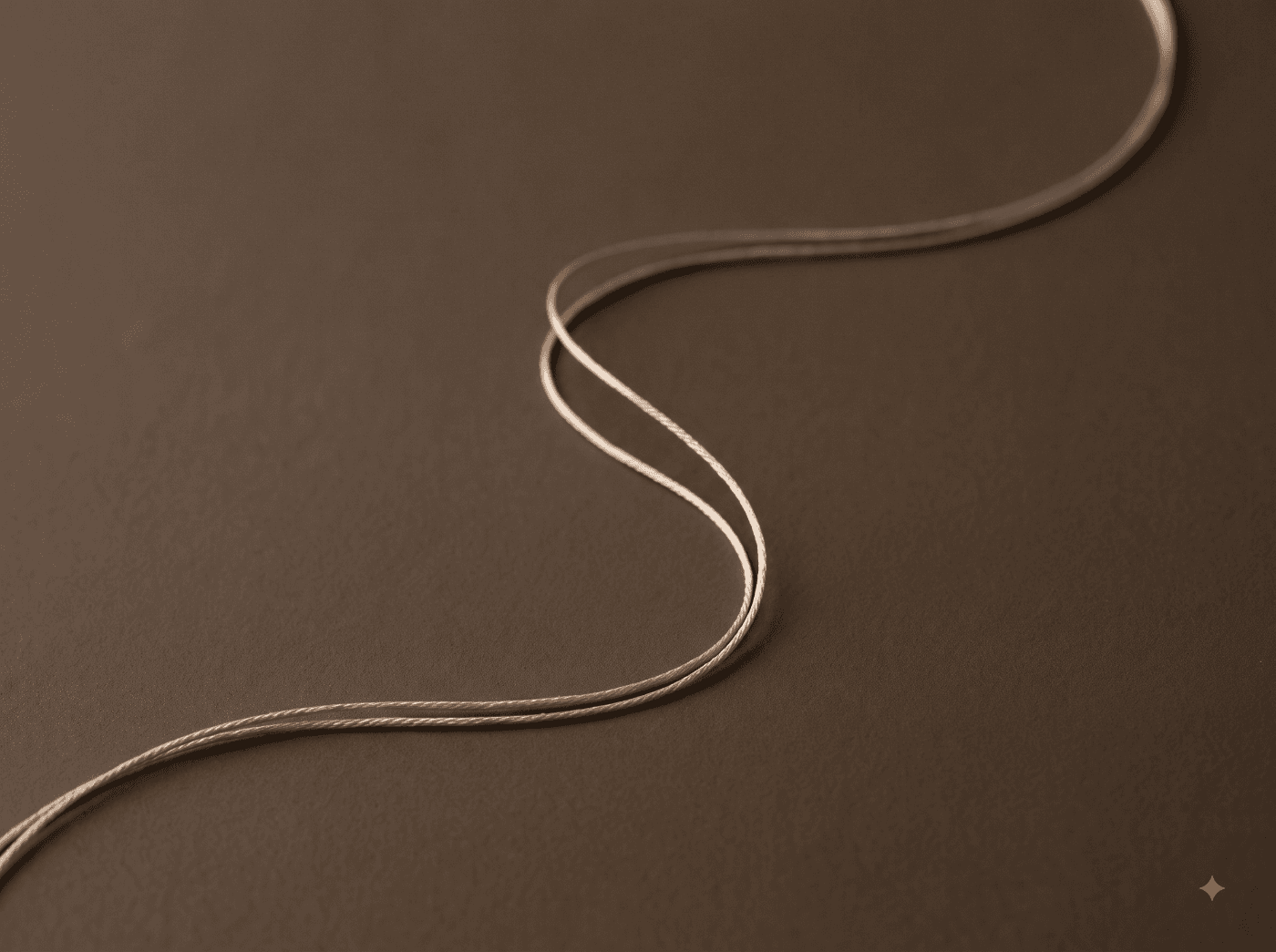 Thread curving in a calligraphic line on a dark taupe background